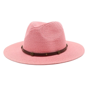 Detail of pink straw fedora hat featuring a brown faux leather band with metallic studs