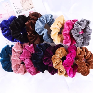 Flat lay of colorful velvet hair scrunchies in various shades on white fabric background