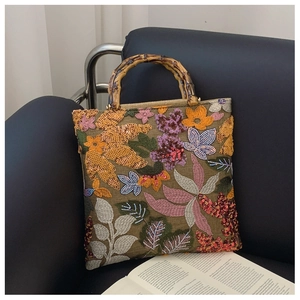 Detailed close-up of floral embroidery and sequins on a linen handbag with bamboo handles