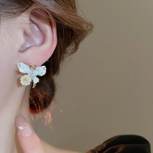 Close-up detail of cream butterfly flower earring on model with golden metal finish