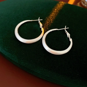 Detailed view of silver matte geometric hoop earrings on dark green velvet background