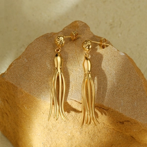 Golden octopus tassel earrings in stainless steel on a natural rock background
