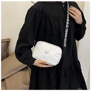 Close-up of a white nylon crossbody bag featuring a butterfly ornament and lettered strap