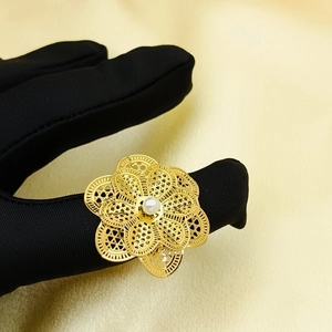 Close-up of golden hollow layered flower ring with pearl on hand with black gloves