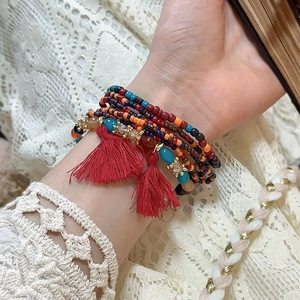 Detail of bohemian multilayer beaded bracelet with vibrant red tassels on the wrist