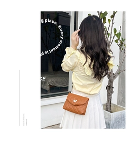 Detail of a brown quilted crossbody bag featuring a white butterfly clasp and gold chain strap