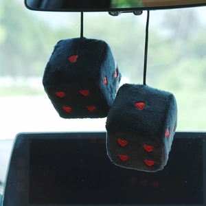 Close-up of black plush car dice with red heart patterns hanging on a rearview mirror