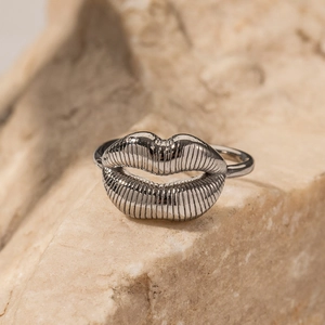Bague ouverte en acier inoxydable argenté avec design de lèvres 3D sur roche beige