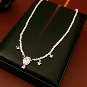 Detailed view of pearl necklace with teardrop and square zircon pendants on a jewelry box