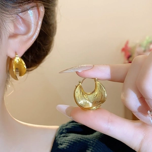Macro shot of gold croissant-style C-hoop earrings with layered metallic texture details