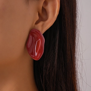 Detailed view of irregular pebble-shaped resin earring in deep reddish-brown on model