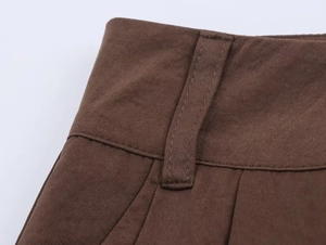 Detail of brown pleated pants showing belt loops and high-quality woven fabric texture