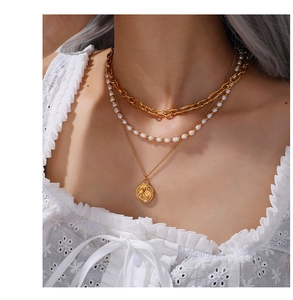 Close-up of layered 18K gold plated necklaces with pearl accents and a round relief pendant