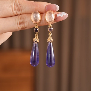 Détail de boucles d'oreilles vintage dorées avec gemmes roses et gouttes en résine violette