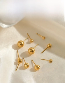 Detail view of golden stainless steel ball stud earrings in various sizes on white silk
