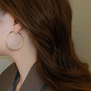 Close-up of a model wearing large gold hoop earrings with a polished metallic finish