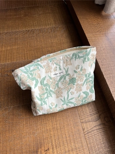 Detail der floralen Baumwolltasche mit Metallreißverschluss und Stoffetikett auf Holz
