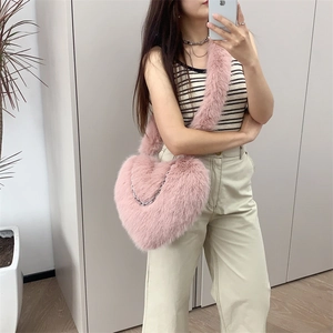Pink heart-shaped plush crossbody bag with silver chain detail shown on a model