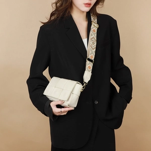 Close-up of beige woven leather crossbody bag with geometric pattern wide strap