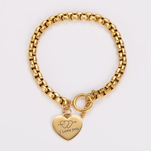 Bracciale a catena spessa dorata con ciondolo a cuore e chiusura OT su fondo bianco