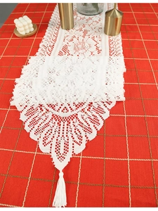 Close-up of white crochet lace table runner with intricate tassels on red checkered cloth