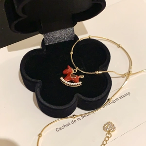 Close-up of gold plated necklace with red pony charm and heart pendant in gift box