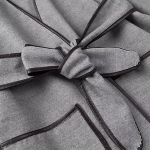 Detail of wool coat featuring dark leather trim piping and a belted waist bow design