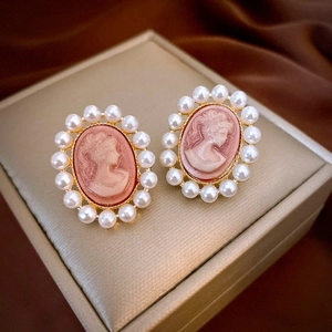 Macro shot of vintage gold-tone cameo earrings with pearl border on luxury velvet
