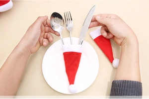 Detailed view of hands placing cutlery into a red non-woven mini Christmas hat holder