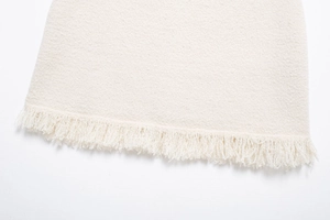 Detailaufnahme von cremefarbenem Tweed-Stoff mit Strickmuster und Fransen-Saum-Details