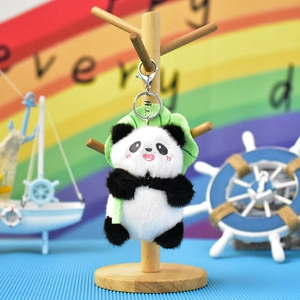 Detailed view of a cute plush panda keychain with a green leaf hood on a wooden stand