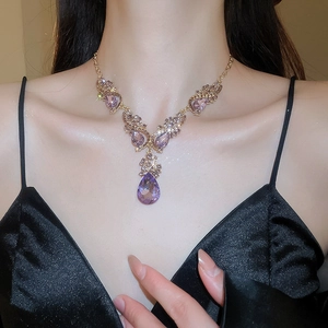 Detailed close-up of a purple teardrop crystal pendant on a gold vintage chain