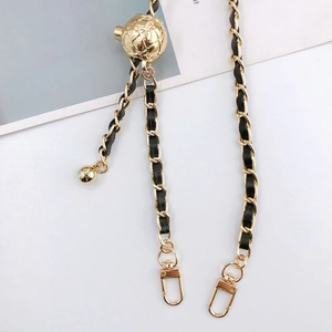 Detail of gold metal chain woven with black leather featuring a spherical charm accessory