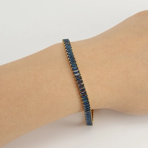 Detail of a gold tennis bracelet featuring rectangular blue zircons worn on the wrist