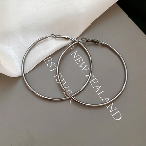 Close-up of high-shine silver hoop earrings on a minimalist textured backdrop
