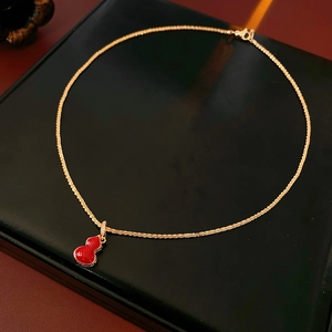 Detail of gold-plated gourd necklace with red pendant and small crystals on a display box