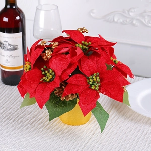 Red artificial poinsettia plant in gold pot on a decorated dining table setting