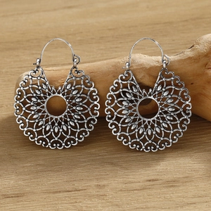 Macro shot of silver vintage hollow mandala earrings on a natural wood surface