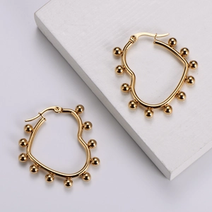 Detail of golden heart-shaped hoop earrings with embedded beads on white display