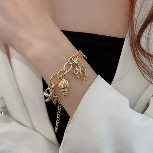 Detail of gold ocean-themed bracelet featuring starfish and shell charms on model wrist