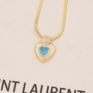 Macro detail of heart pendant with sky blue stone, white crystals and gold snake chain