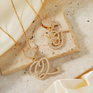 Golden initial necklace with heart design and white cubic zirconia on stone background