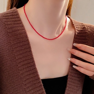 Gros plan d'un collier choker minimalist avec perles rouges porté sous une lumière chaude