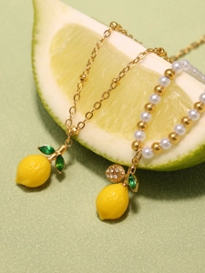 Dettaglio della collana di perline con ciondolo a limone e perle su sfondo di limone fresco