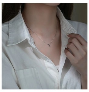 Macro detail of minimalist silver bean pendant necklace on model wearing a white shirt
