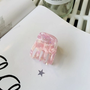 Pince à cheveux en acétate marbré rose pour queue de cheval haute posée sur un livre blanc