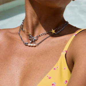 Dettaglio della collana in acciaio con maglie a graffetta, perle e ciondolo a fiocco