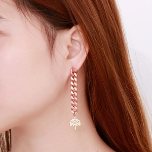 Detail of rose gold long chain earrings featuring a tree of life charm on a model