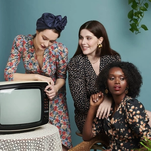 Drei Models in Vintage-Blumenkleidern und stilvollen blauen Turbanen mit Retro-TV-Requisiten