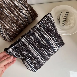 Flat lay of retro textured tweed makeup bag in brown and navy blue with lifestyle props
